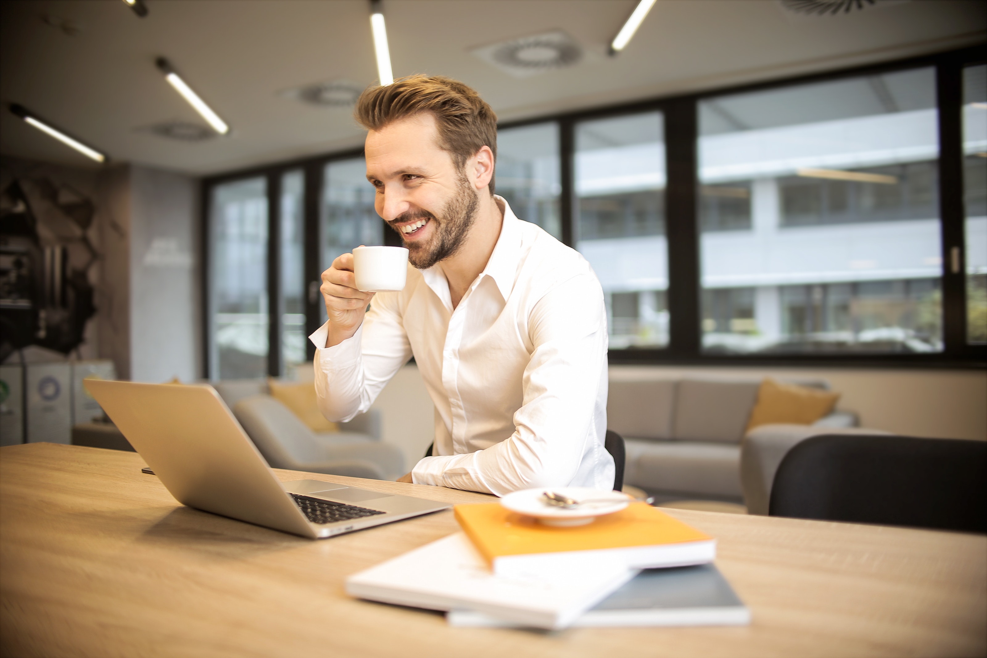 Smiling man enjoying coffee while working on a laptop, embodying job satisfaction