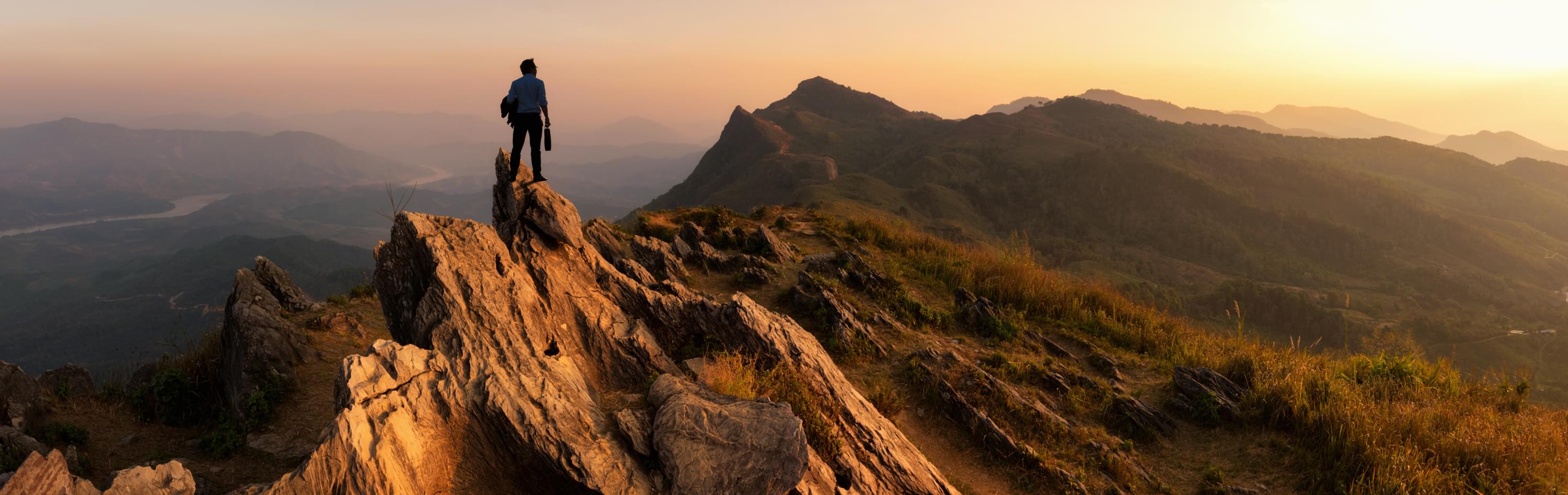 Person standing atop a mountain ridge at sunset, reflecting on personal and professional growth and the journey ahead