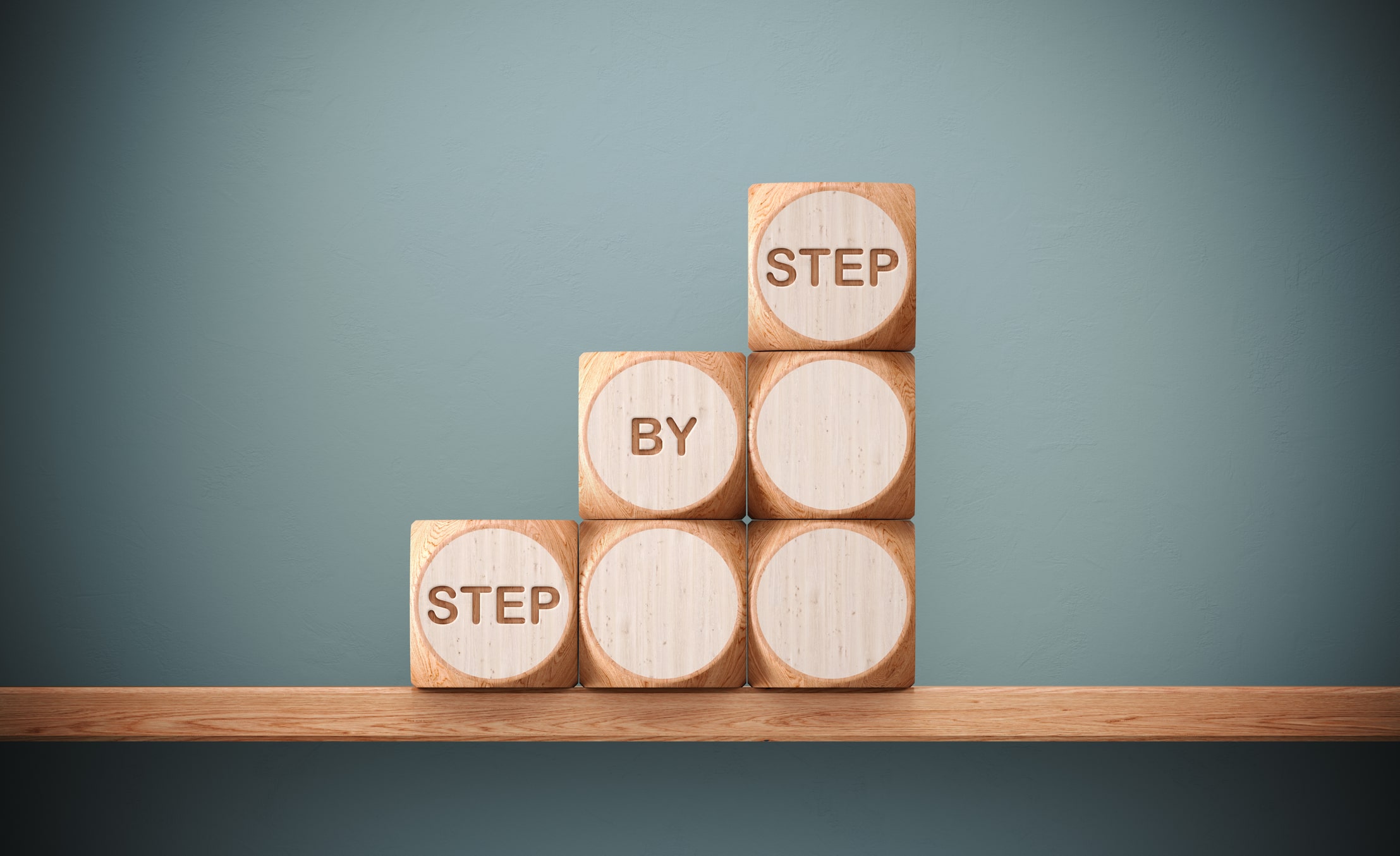 Wooden blocks on a shelf spell out 'STEP BY STEP', symbolizing the structured approach to achieving success