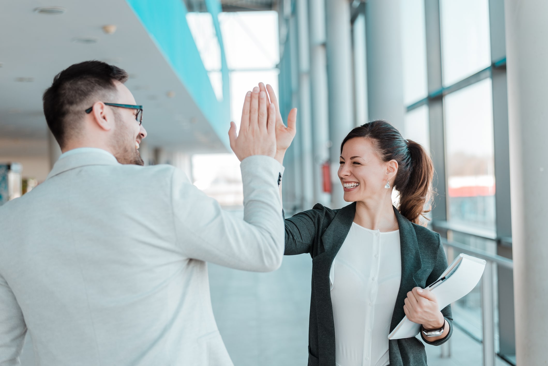 Professionals celebrating success with a high-five in an office environment.